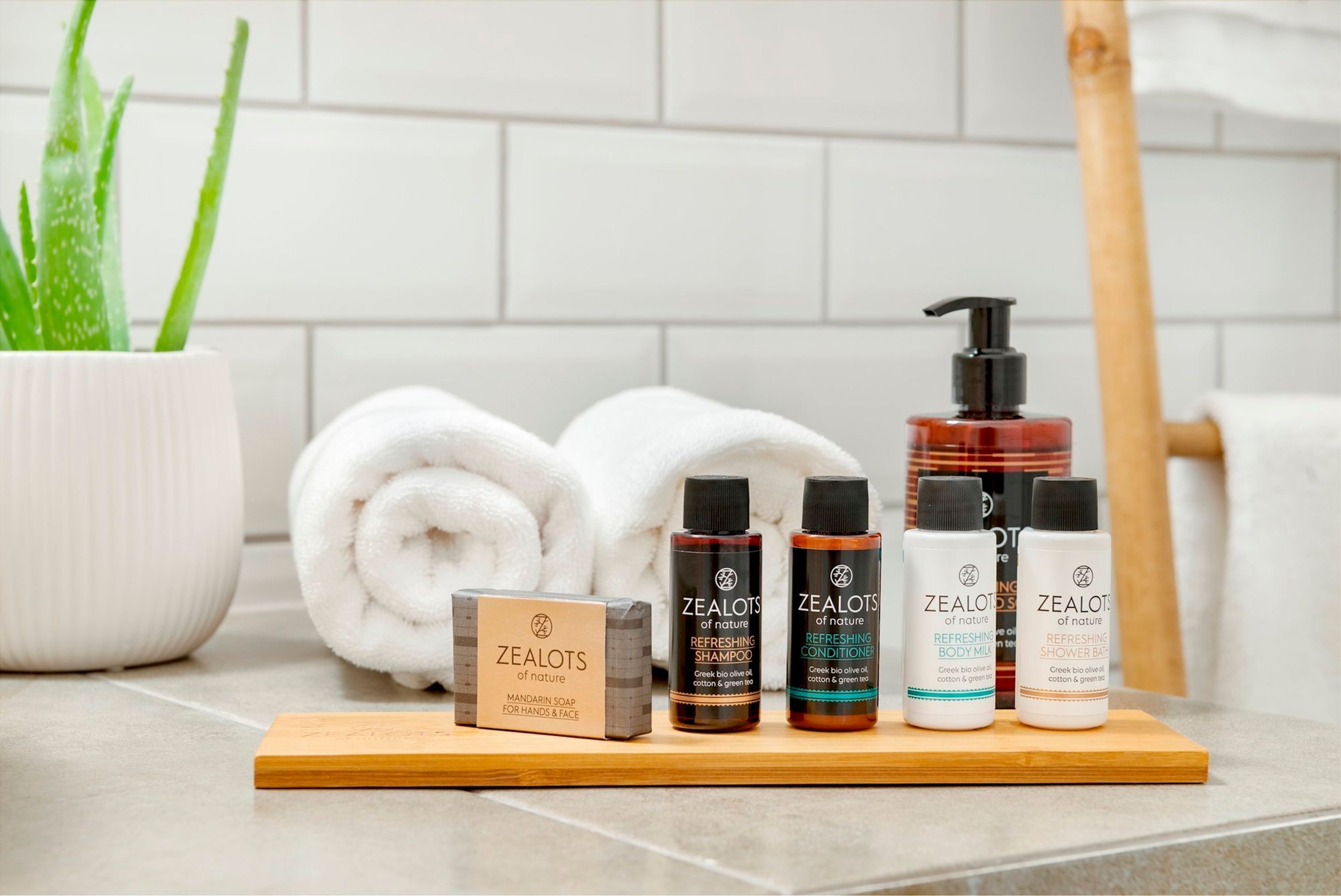 A bathroom with a white towel, aloe vera plant, and various Zealots of nature products on a wooden tray.