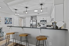 Une cuisine moderne avec des meubles blancs, un plan de travail noir et trois tabourets de bar en bois.