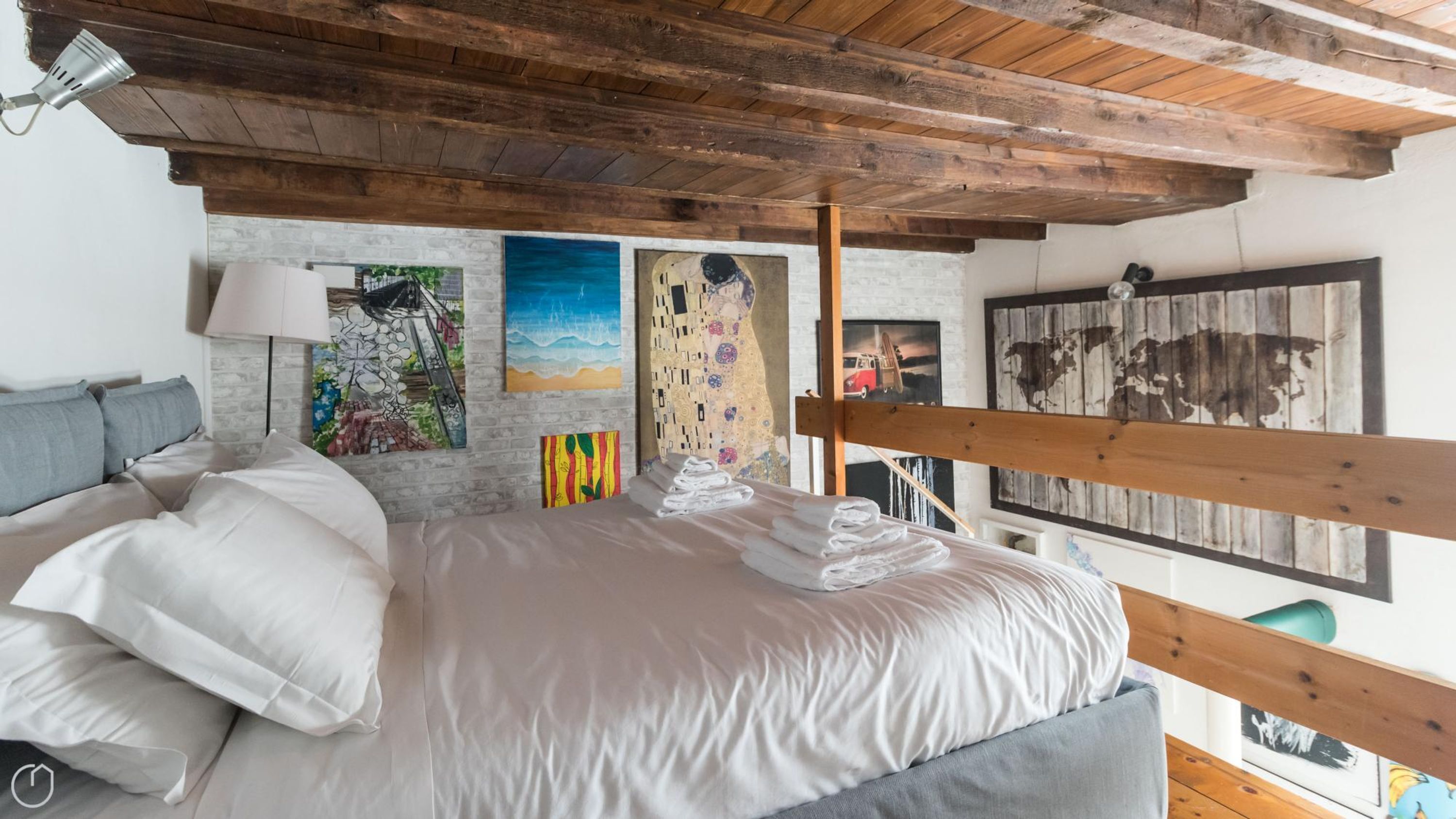 Une chambre avec un lit, un lit superposé en bois, une lampe et des œuvres d’art accrochées aux murs.