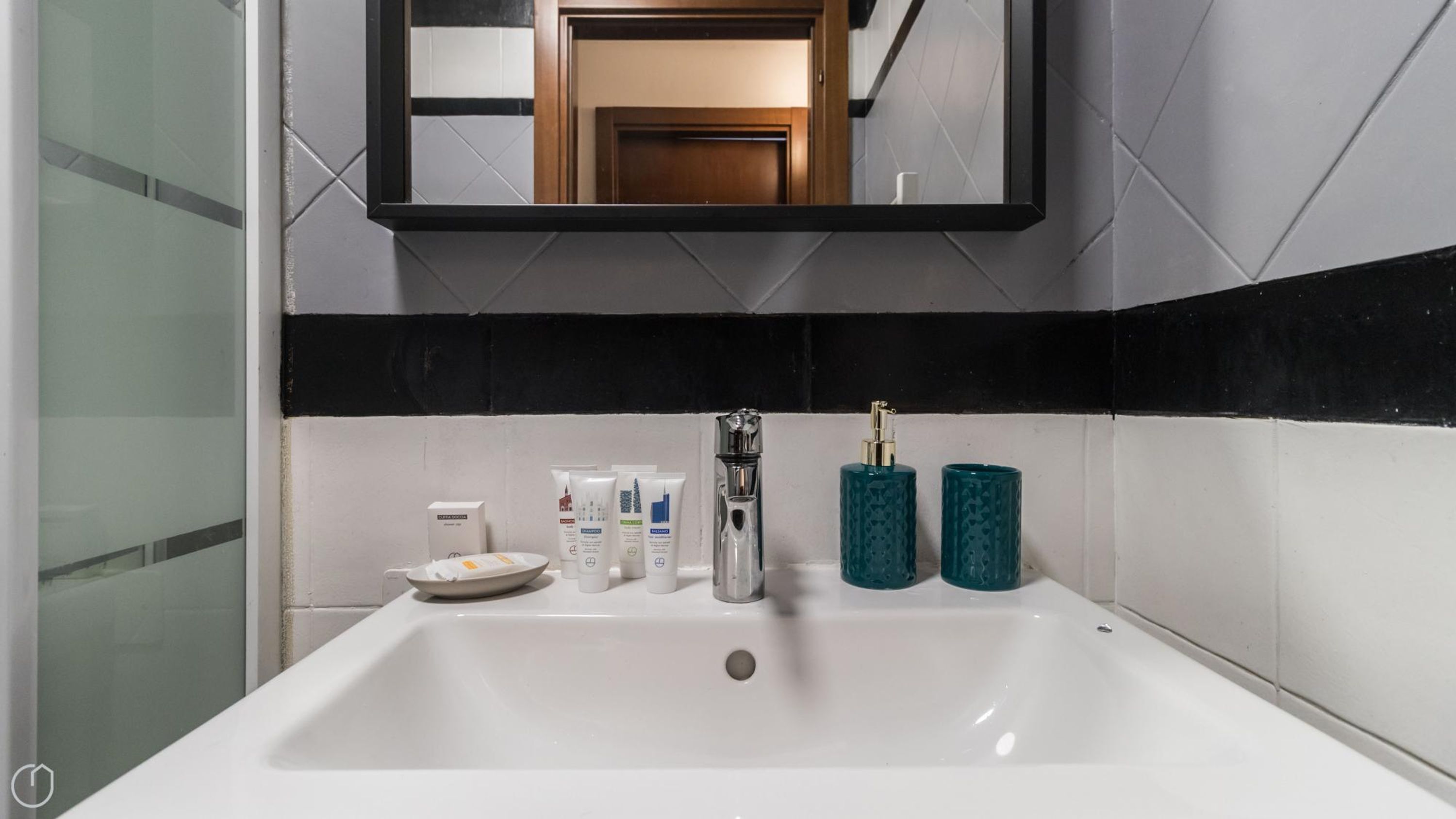 Un baño con un lavabo blanco, un espejo encima y artículos de aseo en la encimera.