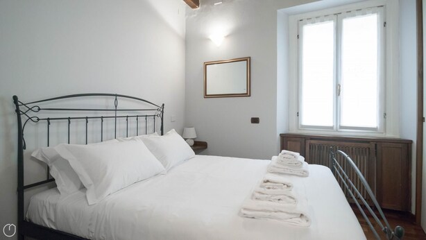 A neatly made bed with white linens and towels, a bedside lamp, a window with blinds, and a radiator. - Italianway Easy - San Calocero 29 (Milan)