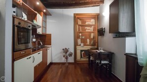 A compact kitchen with wooden cabinets, a built-in oven, and a dining area with a table and chairs. - Italianway Easy - San Calocero 29 (Milan)