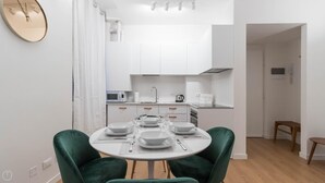 A modern kitchen with white cabinets, a microwave, and a kettle. There is a dining table with plates and glasses set for four. - Italianway Easy - Ripa Ticinese 17 B (Milan)