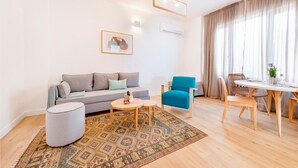 A modern living room with a sofa, a round table, a blue armchair, and a patterned rug. - Premium Deluxe Apartment -c2-common Terrace (Piraeus)