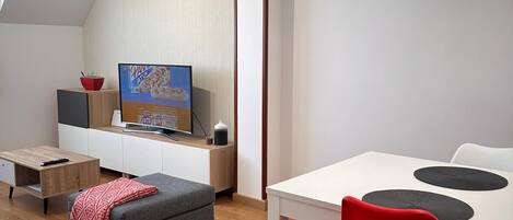 A modern, well-lit room with a dining area, a television, and a cozy seating area.