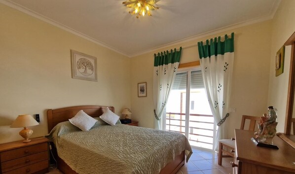 Cozy retreat with a large bed, wooden nightstand, and desk for work and relaxation.