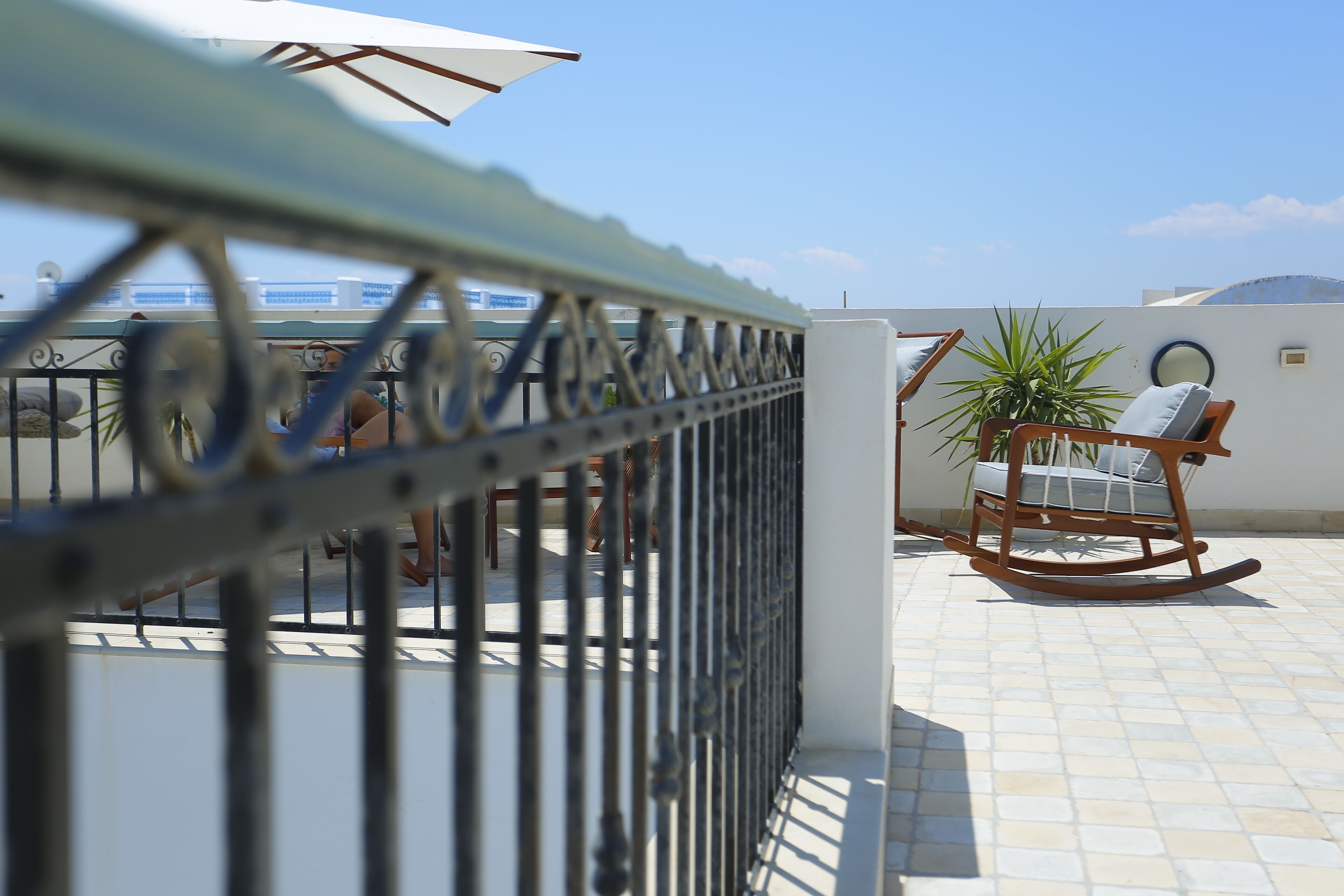Una terrazza con ringhiera in metallo, una poltrona a dondolo e una pianta in vaso.