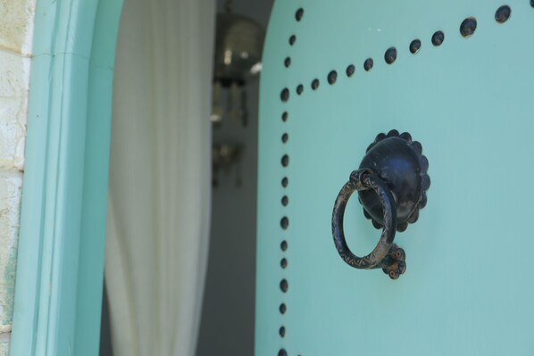 A teal-colored door with a decorative metal handle and a series of circular holes.