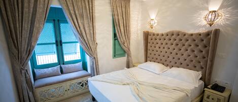 A bedroom with a bed, curtains, a nightstand, and a wall-mounted light fixture.