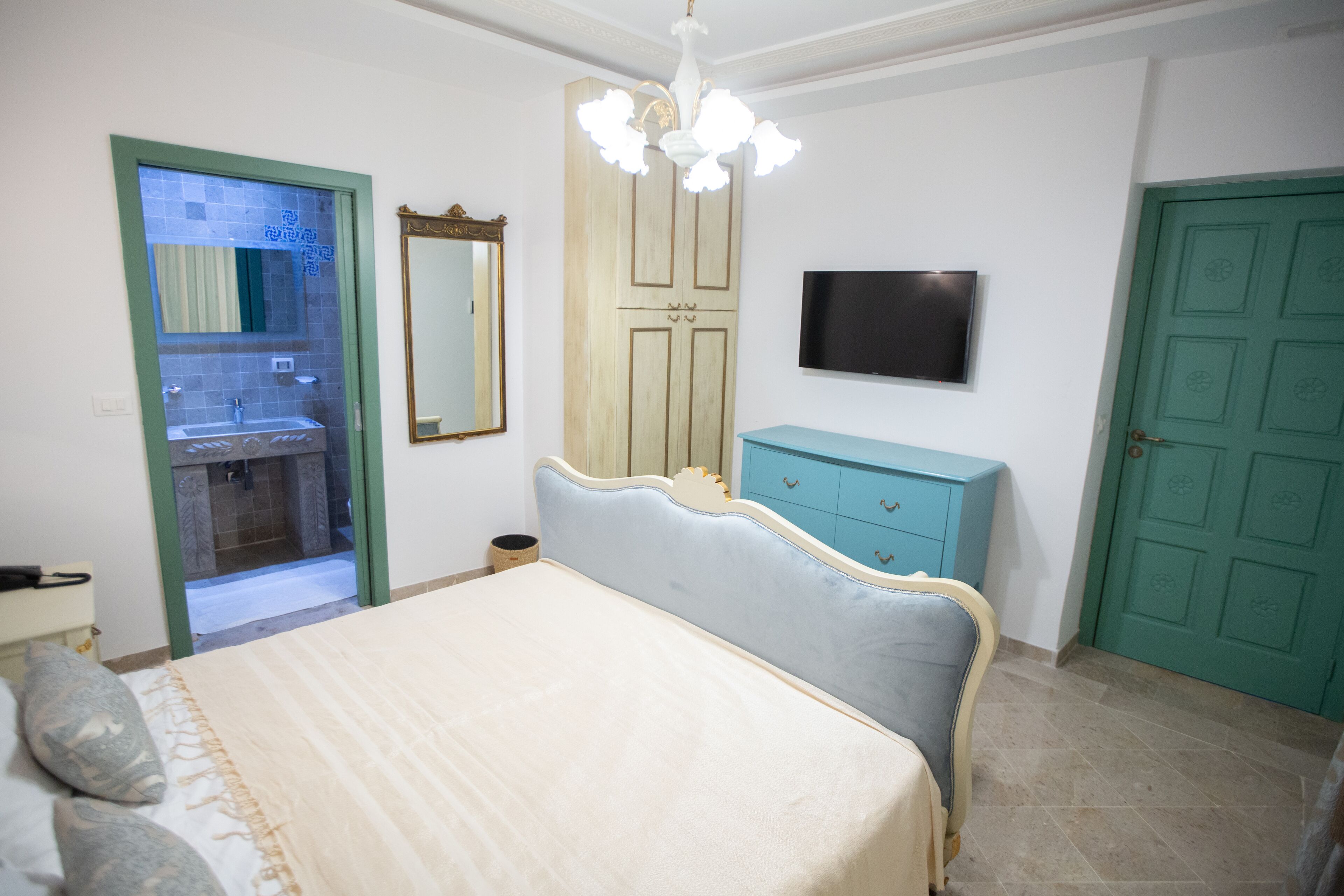 Un dormitorio con cama, cómoda, espejo, televisor y una puerta verde.