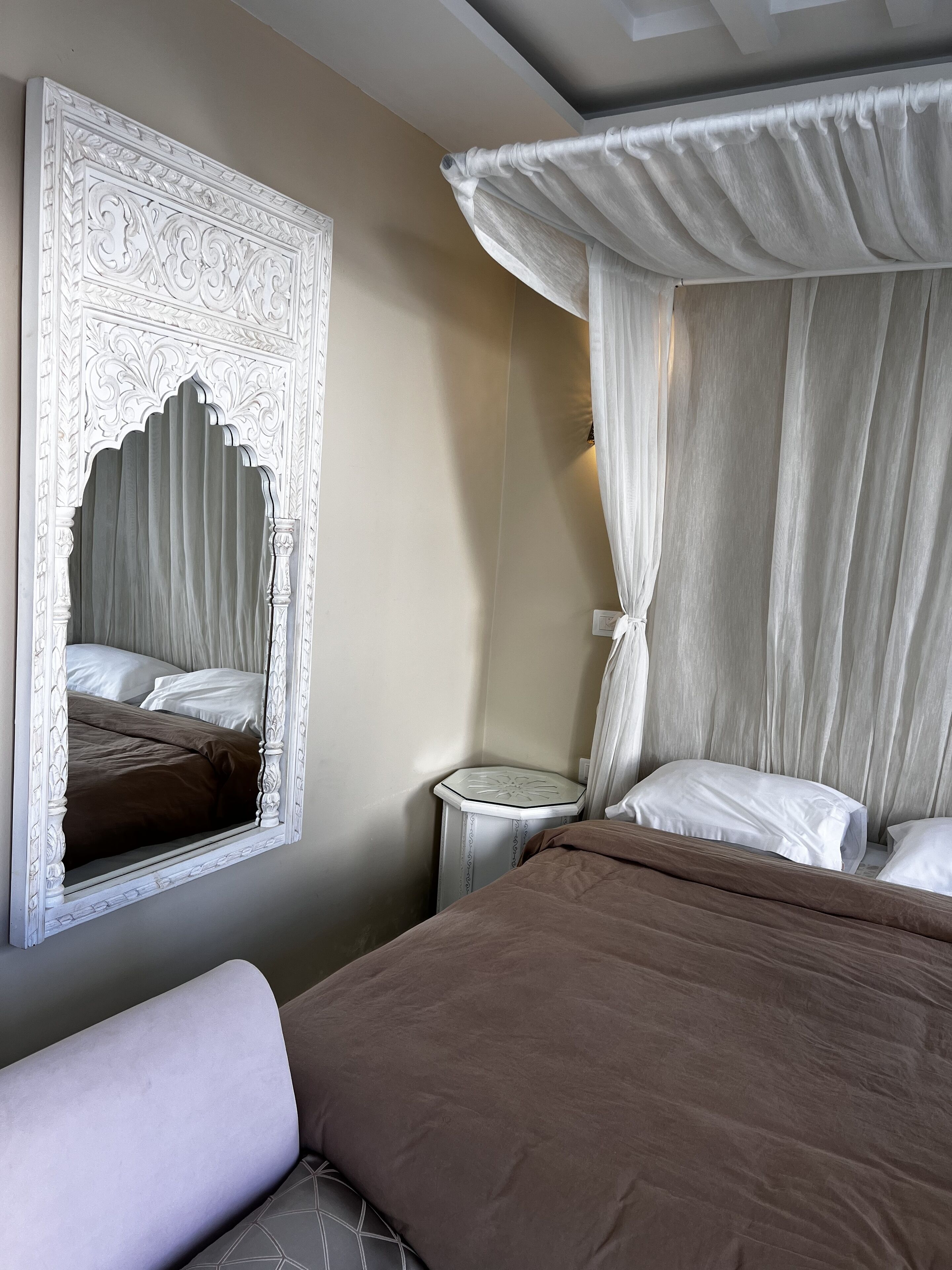 Un dormitorio con un espejo grande y ornamentado, una cama con cabecera marrón y una mesita de noche.