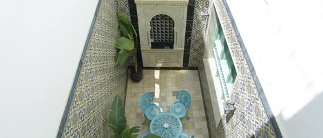 A narrow courtyard with a tiled floor, a decorative archway, and a blue table and chairs arrangement.