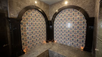 A room with a tiled wall featuring a geometric pattern, a marble bench, and a dark wooden door.