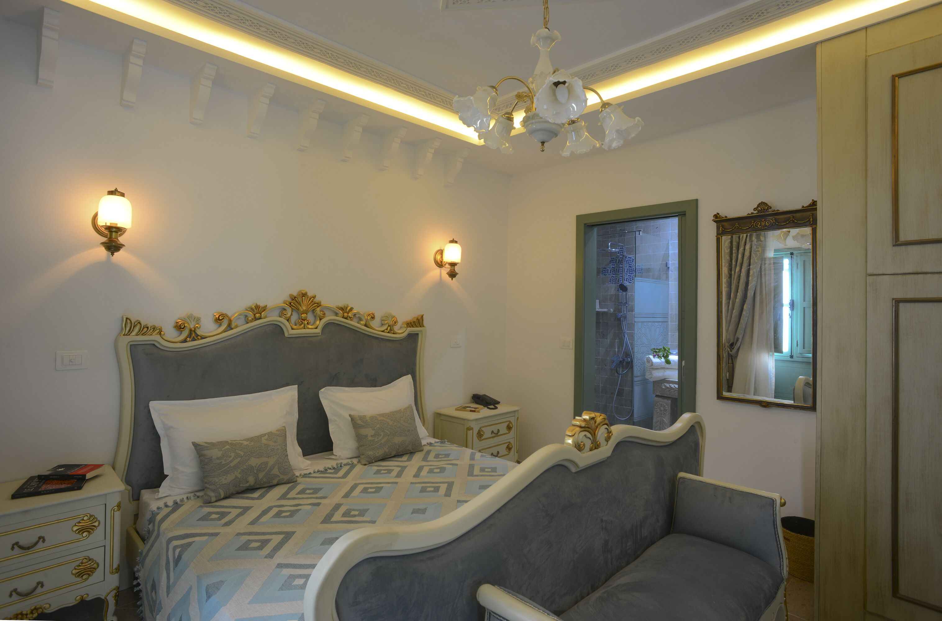 A bedroom with a large bed, two bedside lamps, a chandelier, and a mirror on the wall.