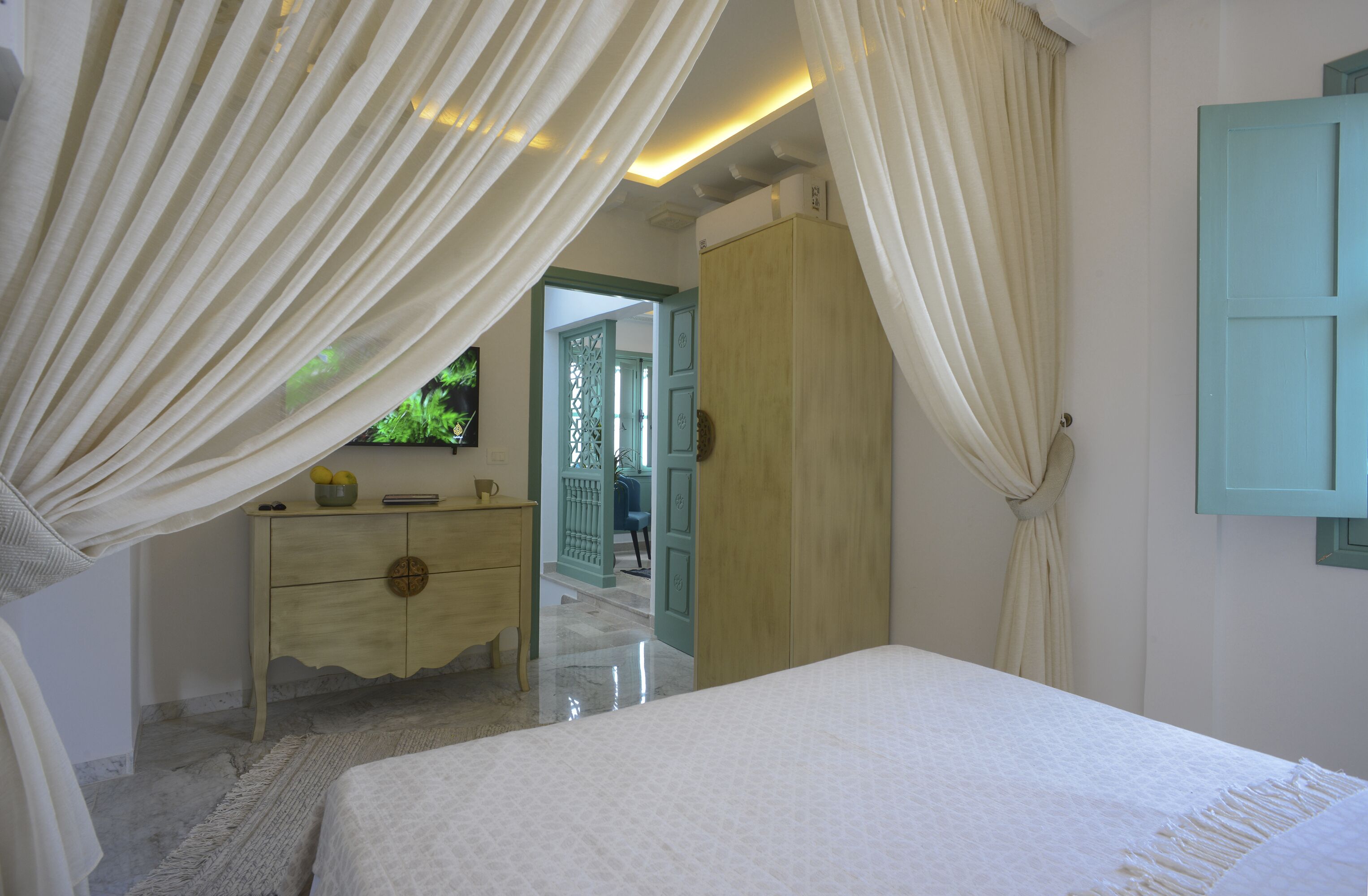 A bedroom with a bed, a dresser, and a wardrobe. There is a door leading to another room.