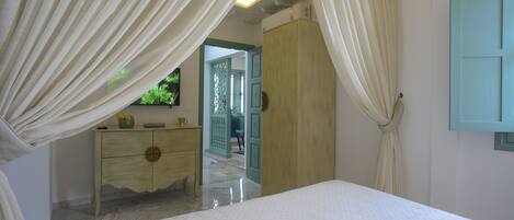 A bedroom with a bed, a dresser, and a wardrobe. There is a door leading to another room.
