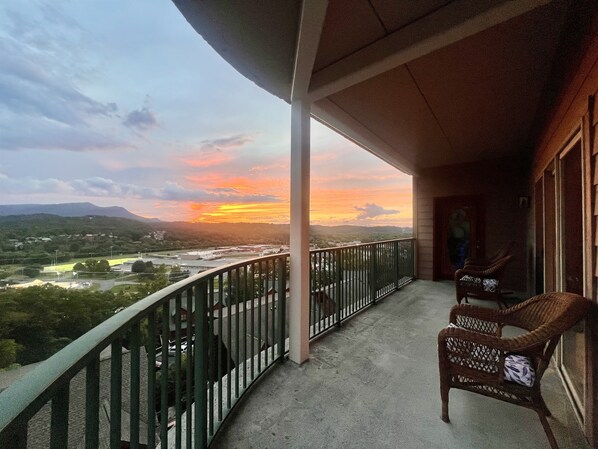 Un balcón con vistas a la puesta de sol sobre un valle, barandilla y dos sillas de mimbre.