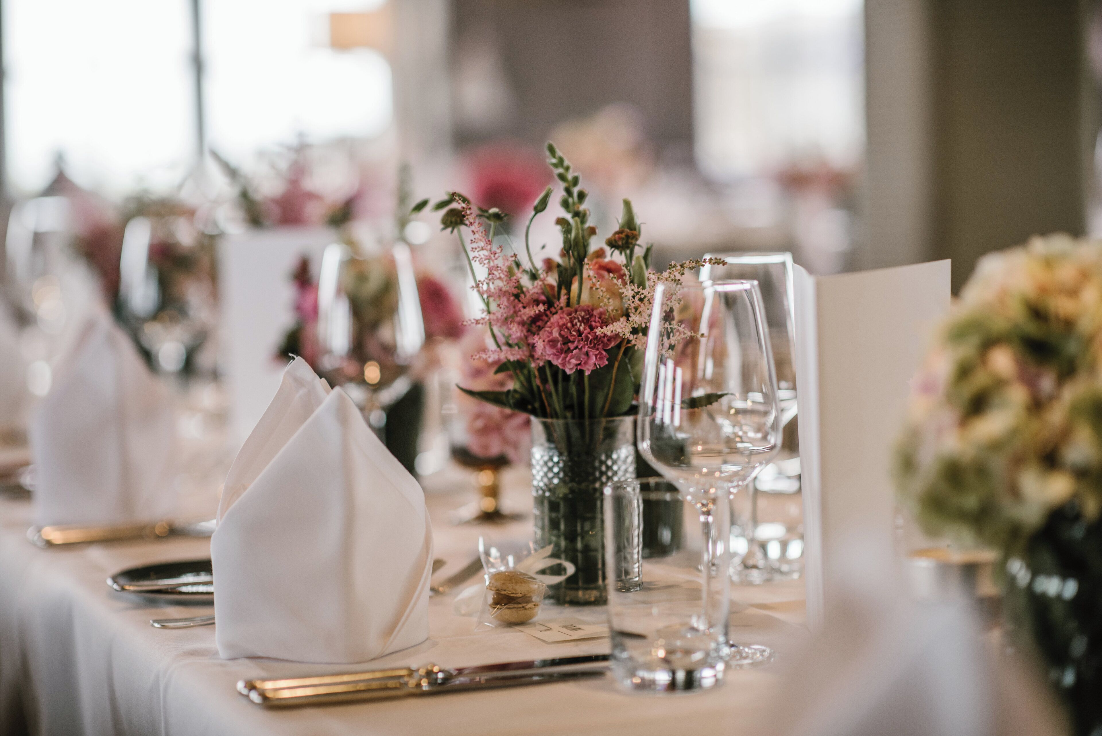 A table set for a formal event with a vase of flowers, clear glassware, and neatly arranged cutlery.