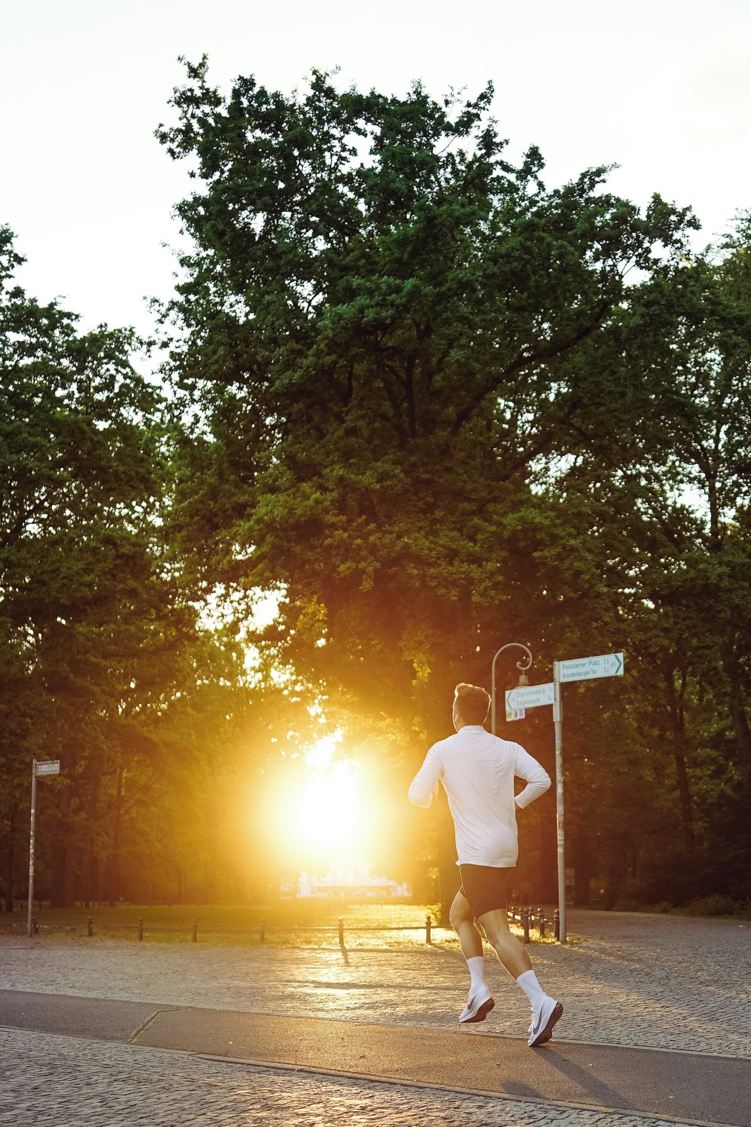 A person jogging on a paved path with a directional signpost in the background.