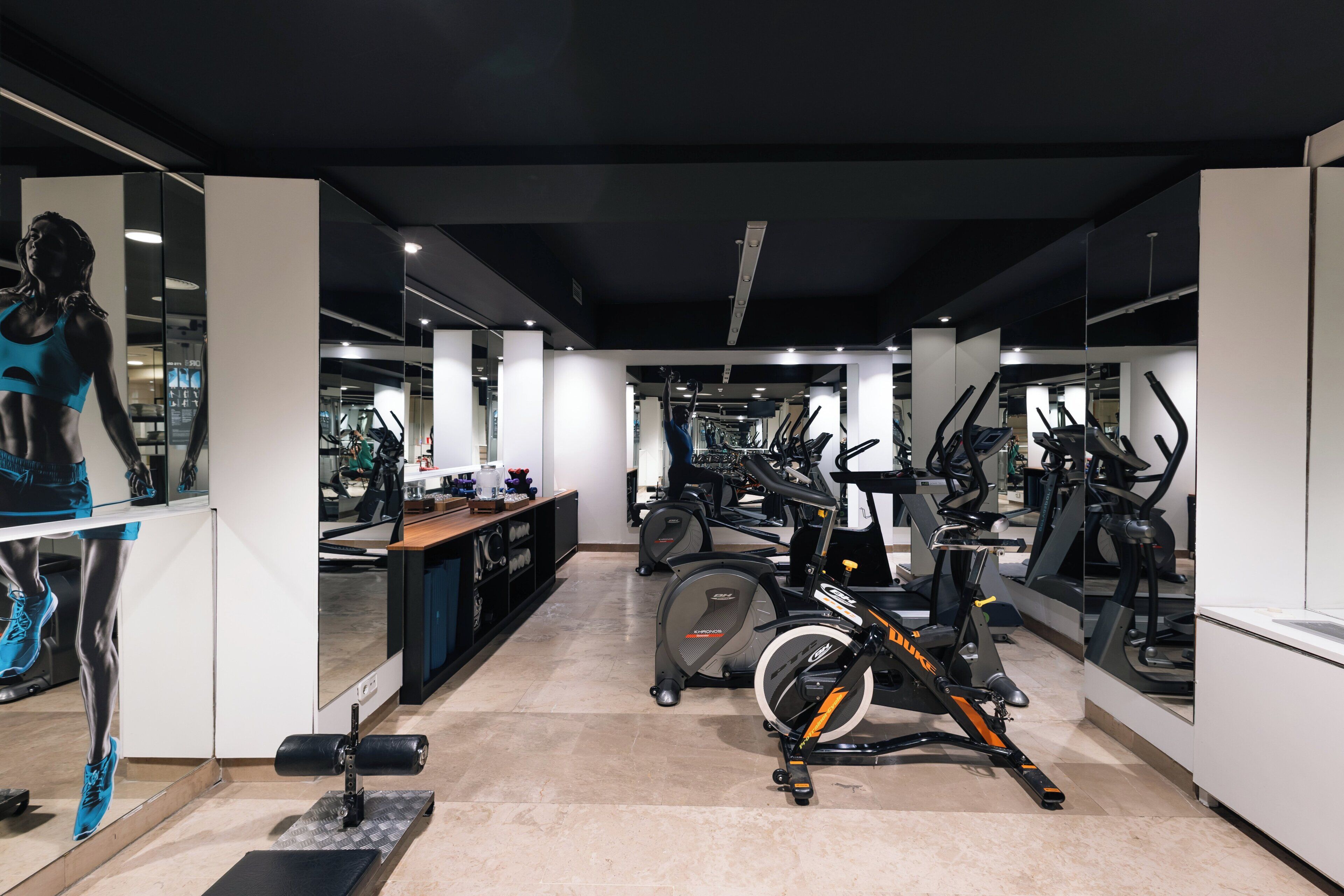 A gym with multiple exercise machines, a mirrored wall, and a display of athletic wear.