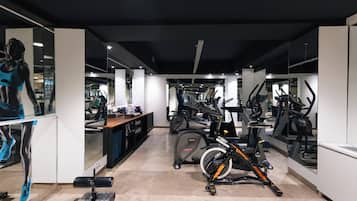 Un gimnasio con varias máquinas de ejercicio, un espejo grande y una exhibición de ropa deportiva.