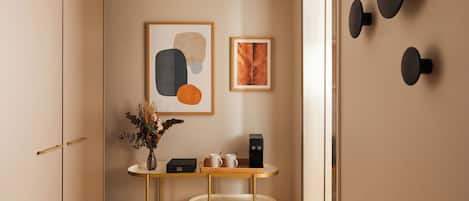 Una habitación moderna con diseño minimalista, que incluye una mesa redonda con un jarrón de plantas secas, una cafetera y dos obras de arte enmarcadas en la pared.