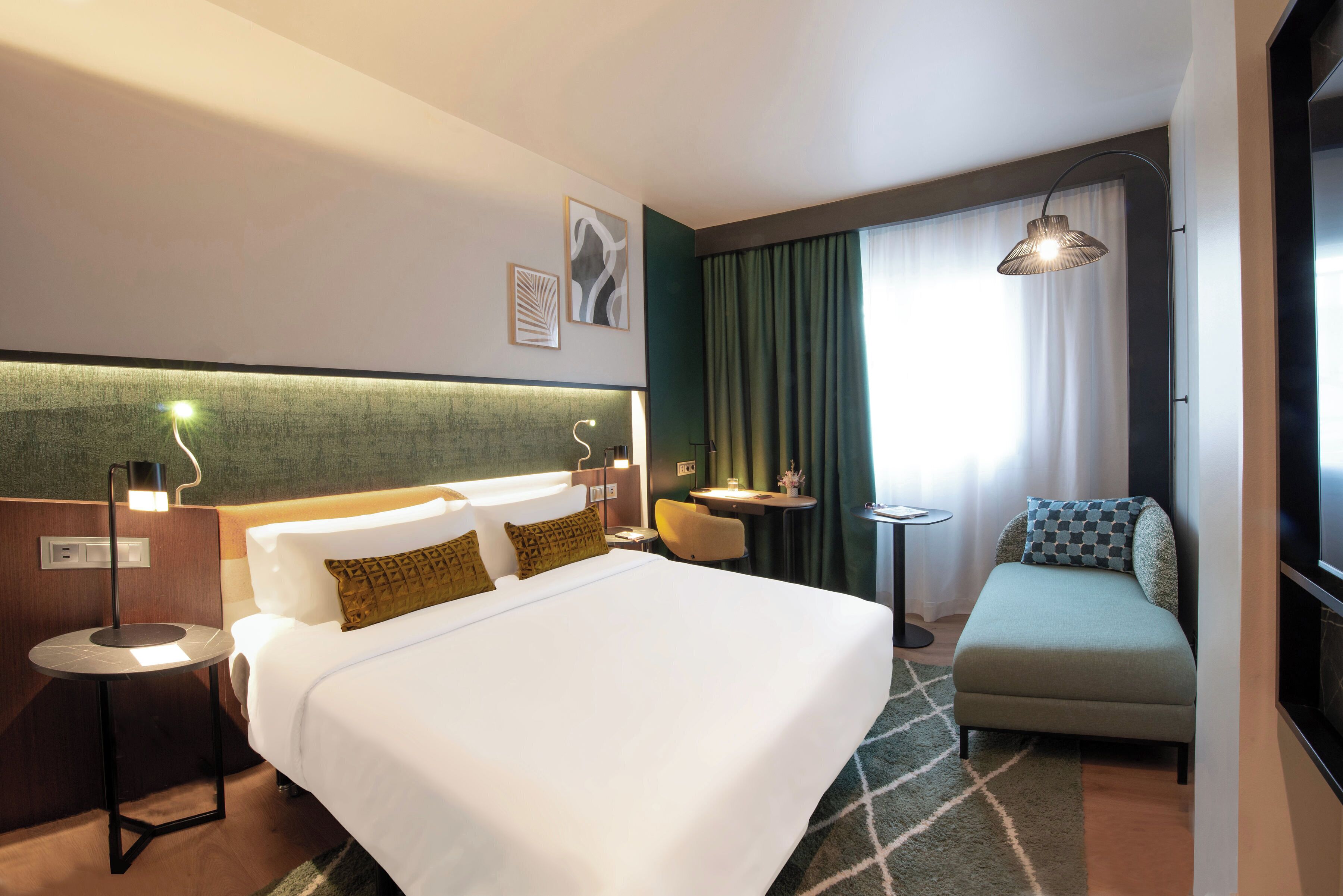 Ein Hotelzimmer mit einem großen Bett, einer kleinen Sitzecke, einem Schreibtisch und einem Fenster mit Vorhängen.