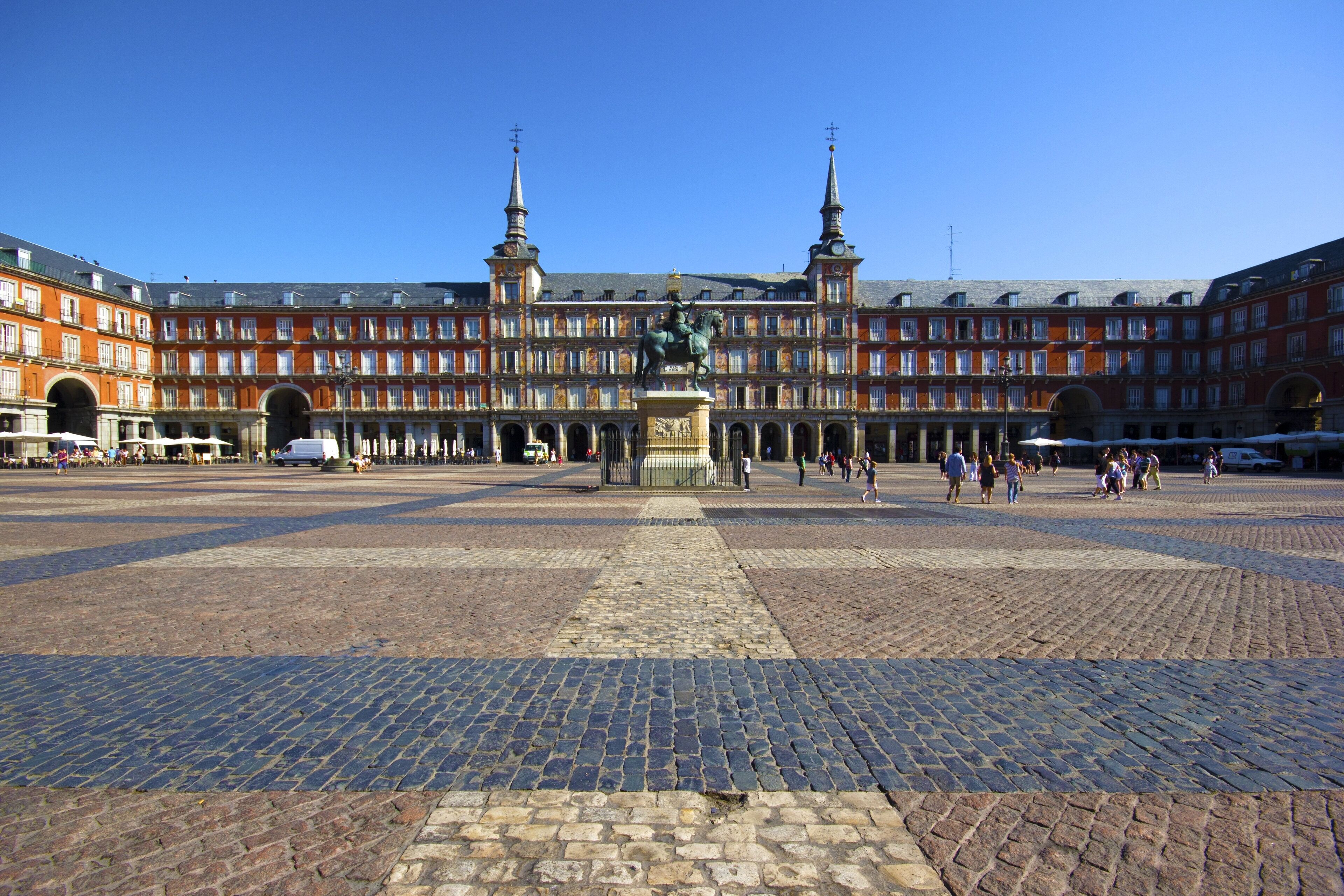 A spacious courtyard with a central fountain, surrounded by historic buildings with multiple floors and arched openings.