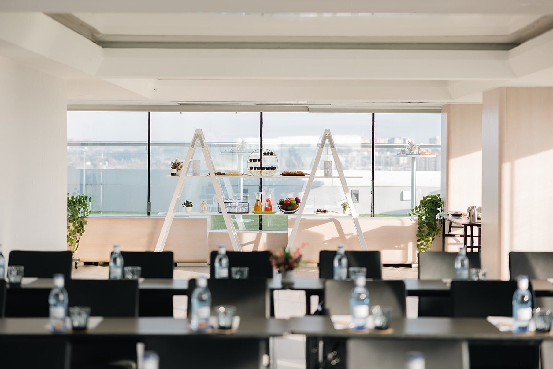 Une salle de conférence moderne offrant une vue panoramique sur la ville, équipée de tables, de chaises et d’un tableau blanc central.