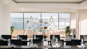 Une salle de conférence moderne offrant une vue panoramique sur la ville, équipée de tables, de chaises et d’un tableau blanc central.