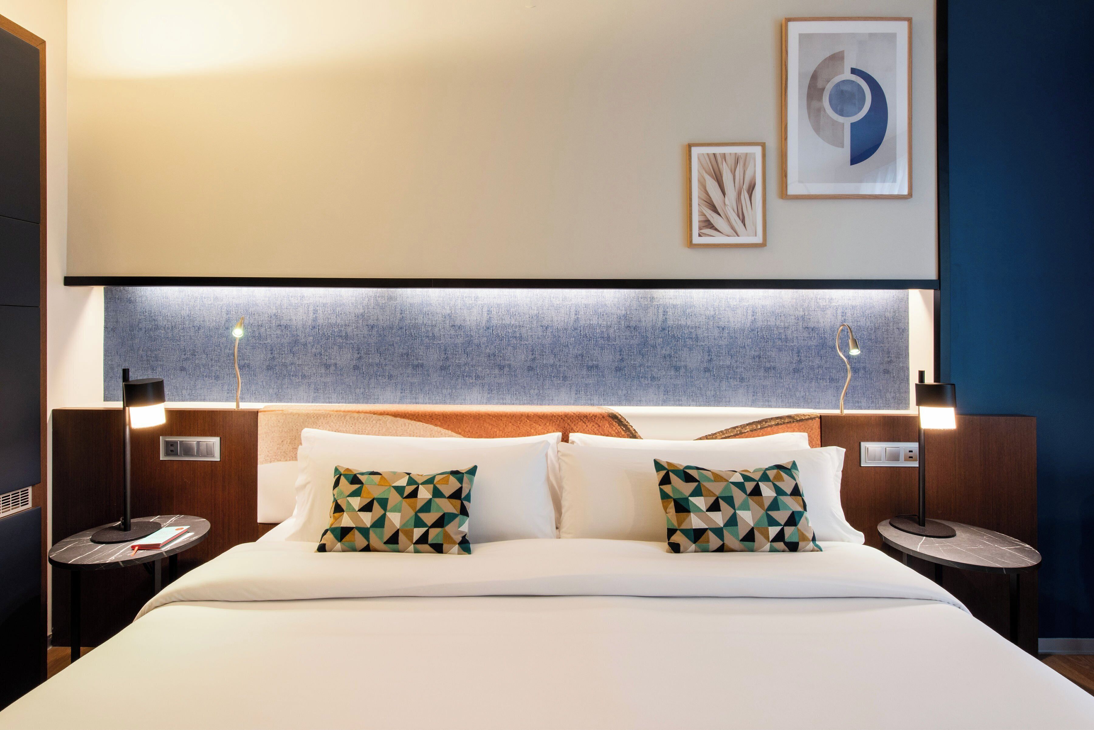 A hotel room with a large bed, two bedside tables, a headboard with a textured design, and wall-mounted artwork.