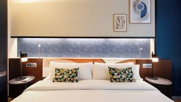 Une chambre d’hôtel avec un grand lit, deux tables de chevet, une tête de lit au motif texturé et des œuvres d’art accrochées au mur.