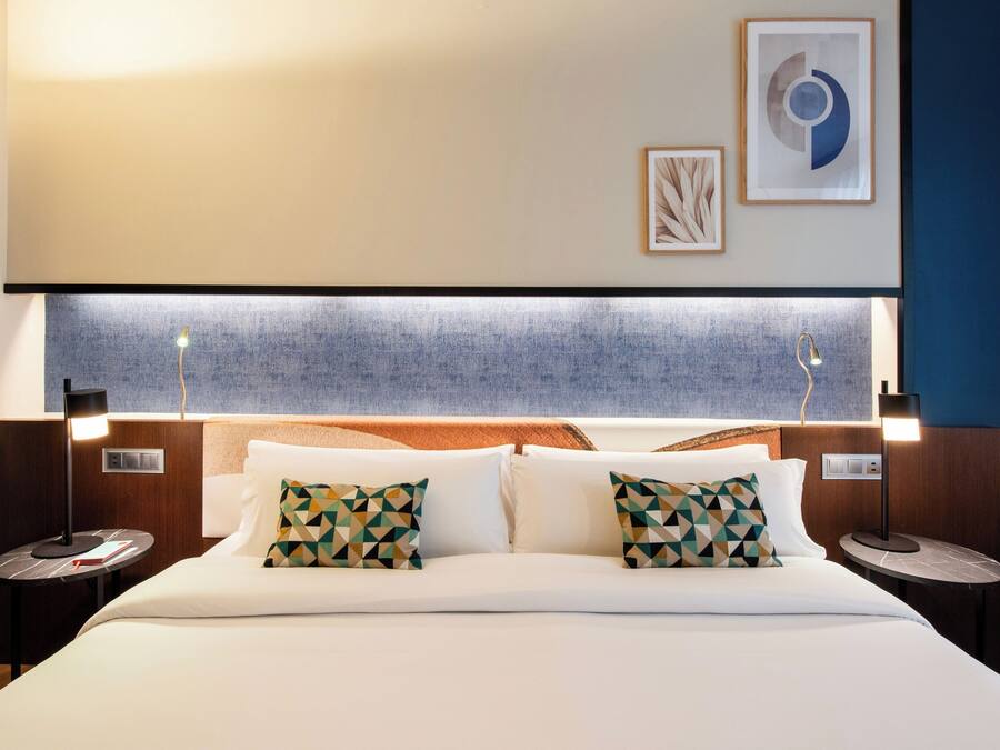 Une chambre d’hôtel avec un grand lit, deux tables de chevet, une tête de lit au motif texturé et des œuvres d’art accrochées au mur.