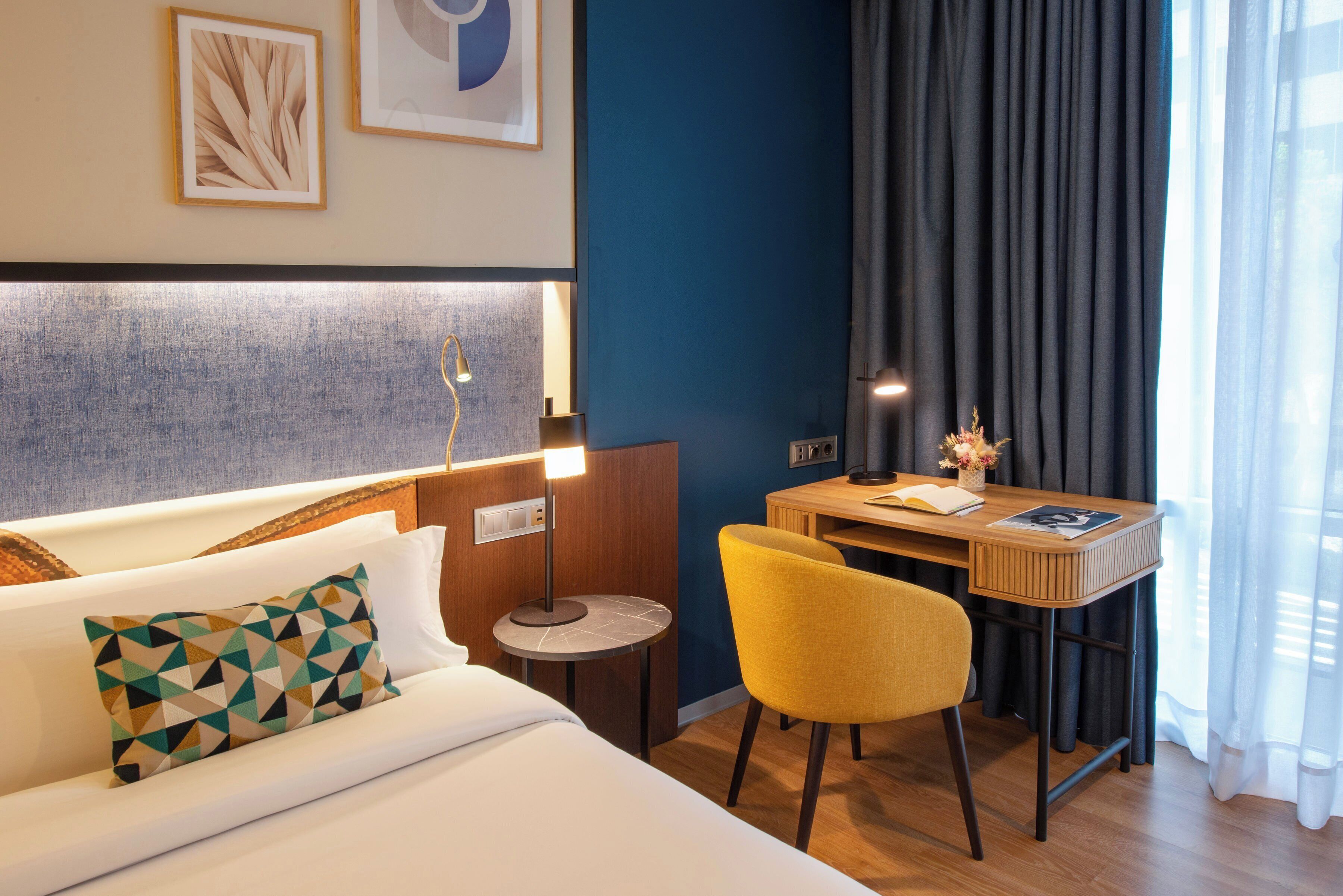 A hotel room with a bed, a desk, a chair, and a small round table.