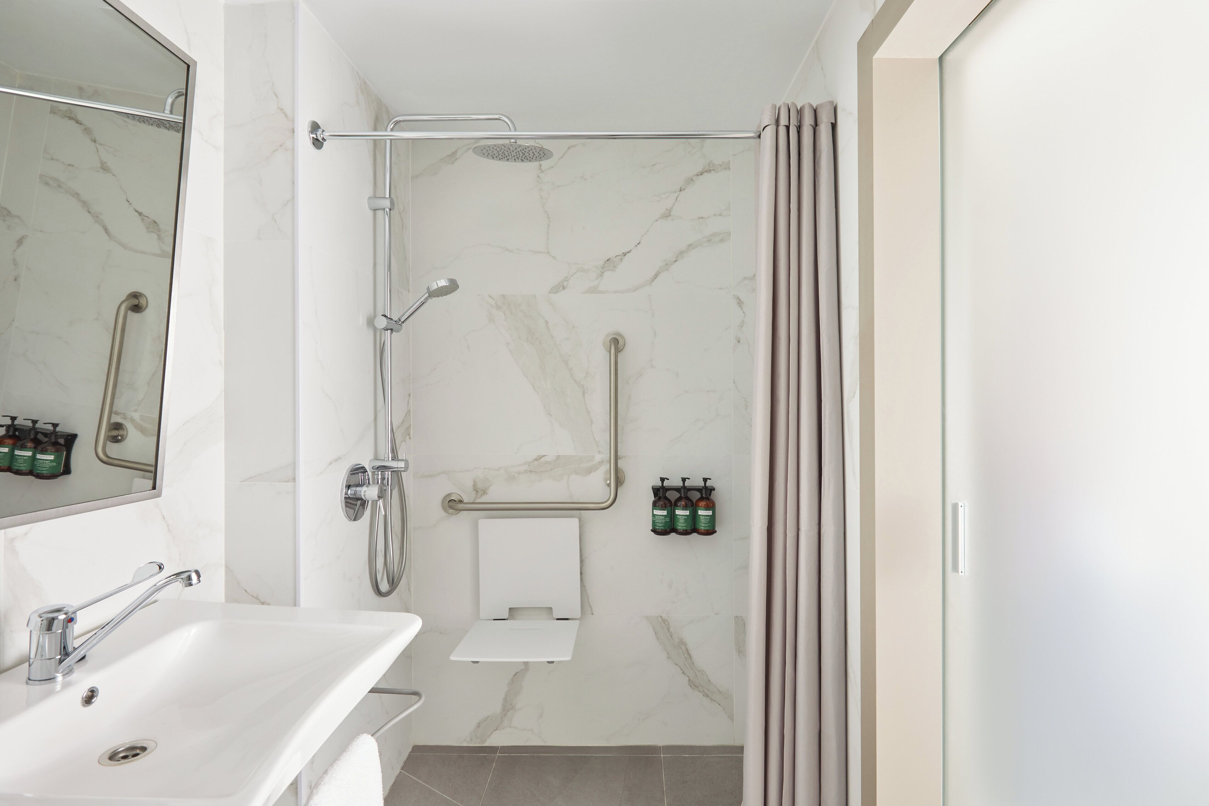 Un baño moderno con lavamanos blanco, cabina de ducha de vidrio y toallero con artículos de aseo.