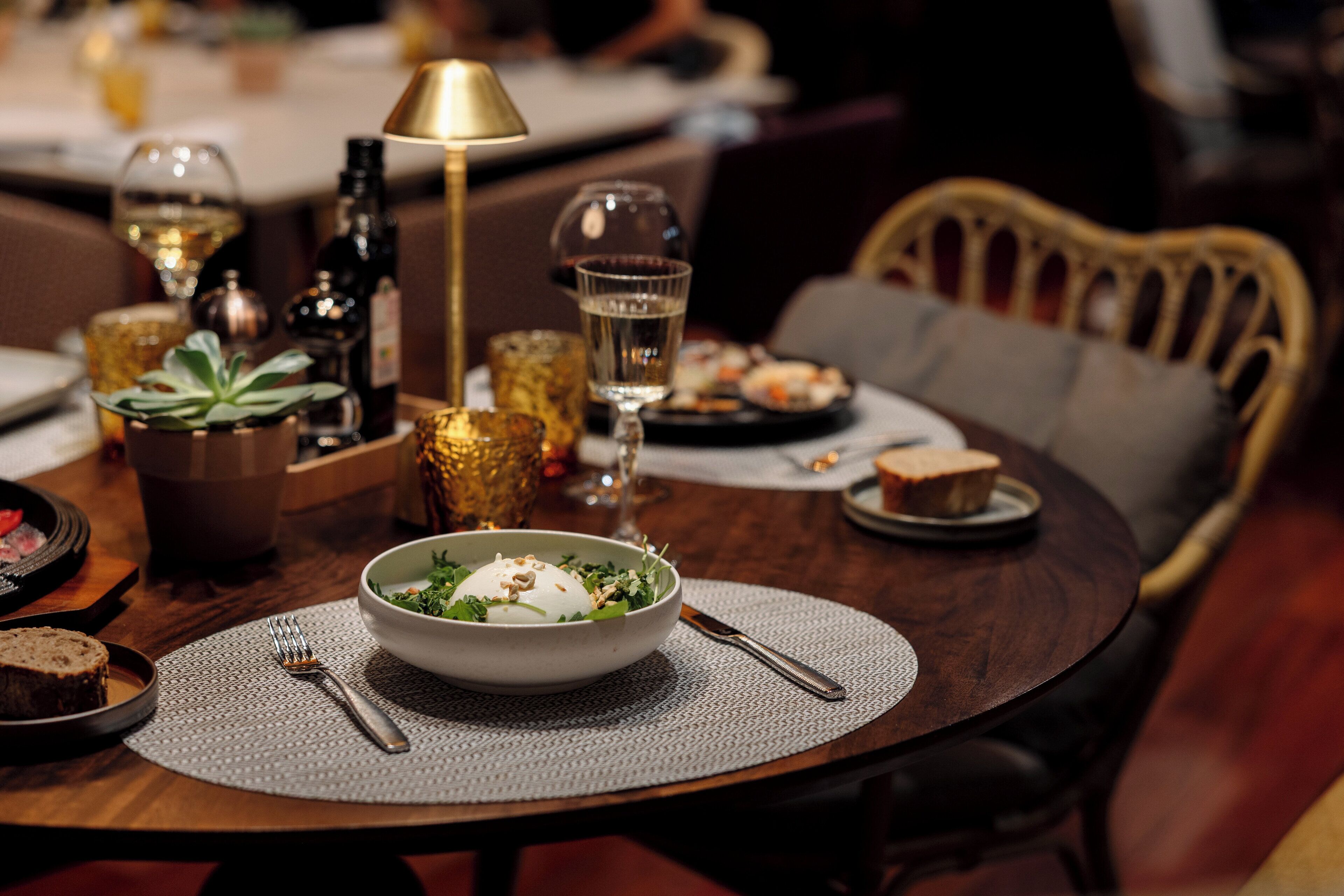 Une table à manger avec un saladier rempli de salade, une bouteille de vin et une bougie.