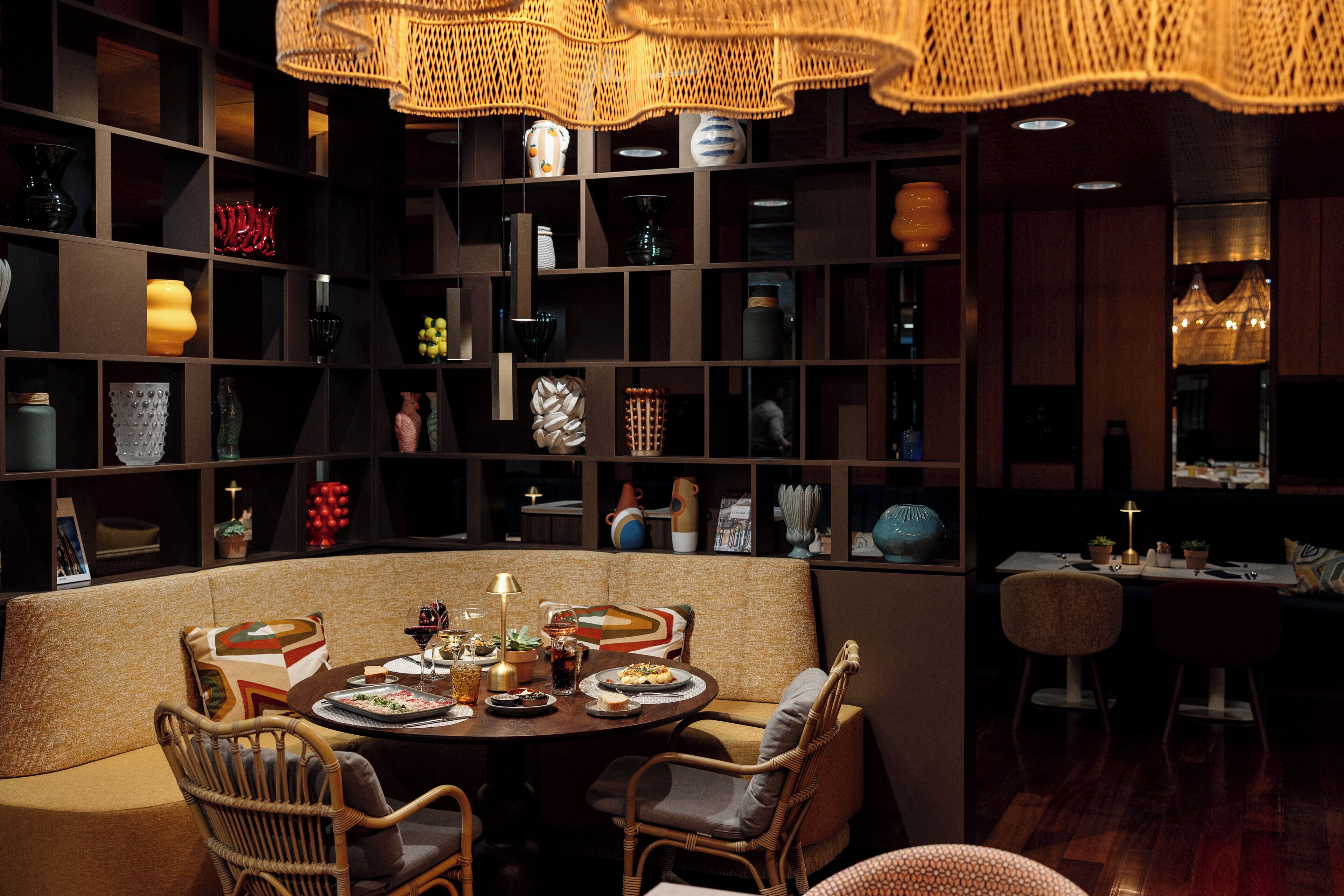 A dining area with a round table, chairs, and a bookshelf filled with various decorative items.