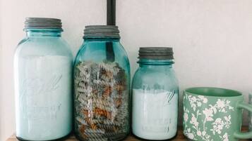 Three glass jars with lids, one containing pasta, another with a white powdery substance, and the third empty. A green floral mug is also visible.