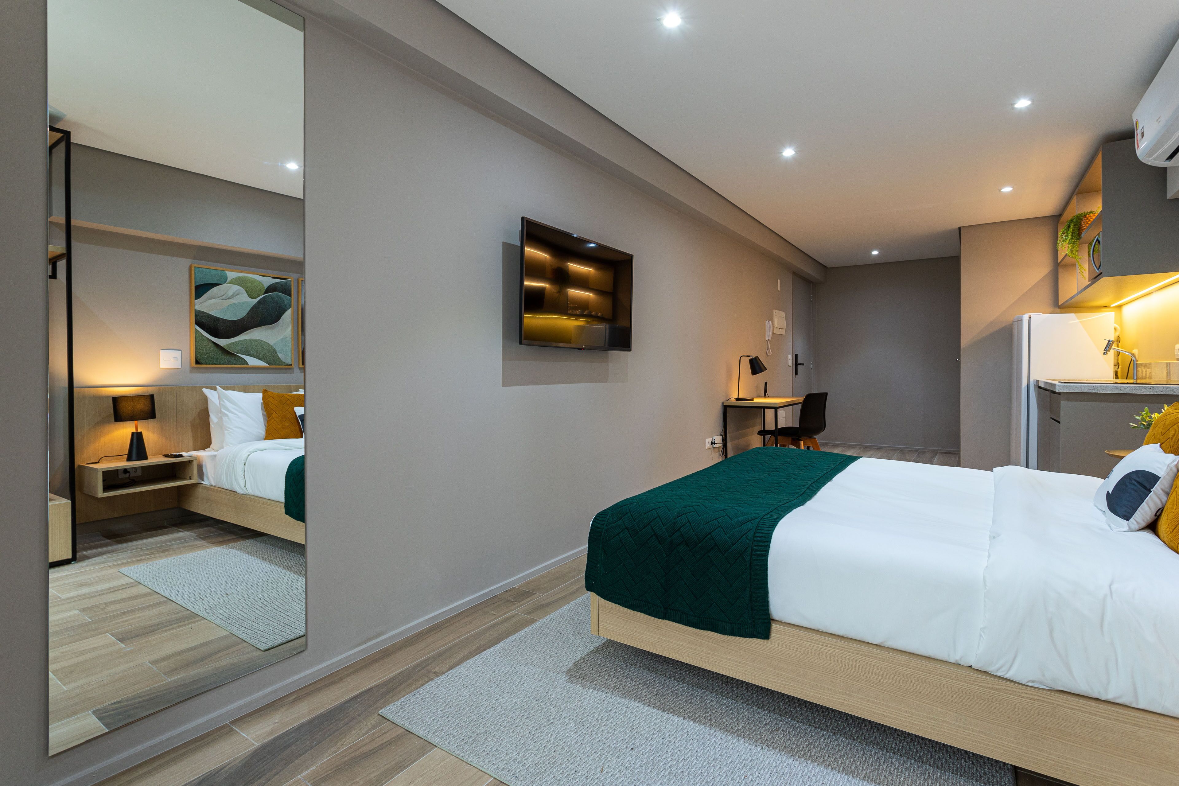 Une chambre d’hôtel moderne avec un grand lit, une table de chevet, un miroir et un petit bureau avec une lampe.