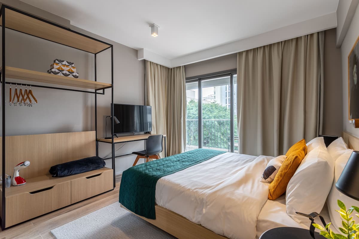 Une chambre d’hôtel moderne équipée d’un lit, d’un bureau, d’une télévision et d’un balcon avec des rideaux.