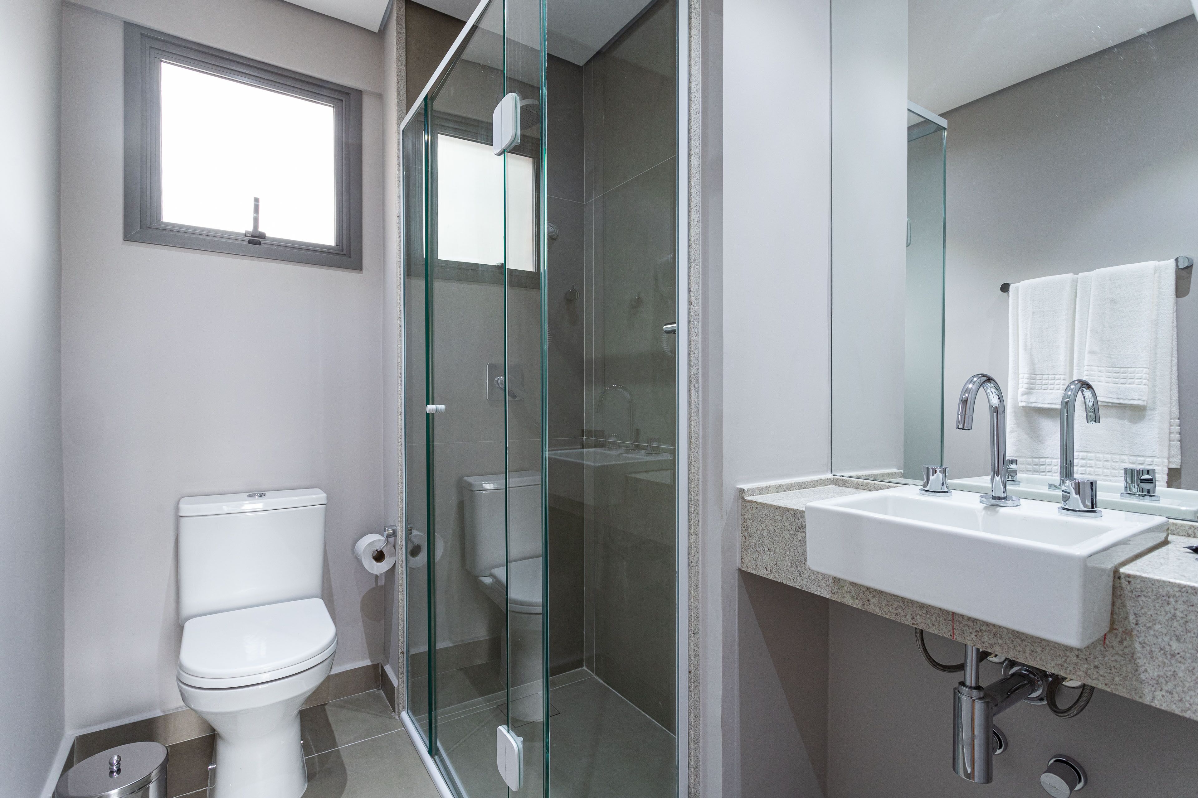 Ein modernes Badezimmer mit einer Glaskabine zur Dusche, einer weißen Toilette und einem Waschbecken mit Spiegel darüber.