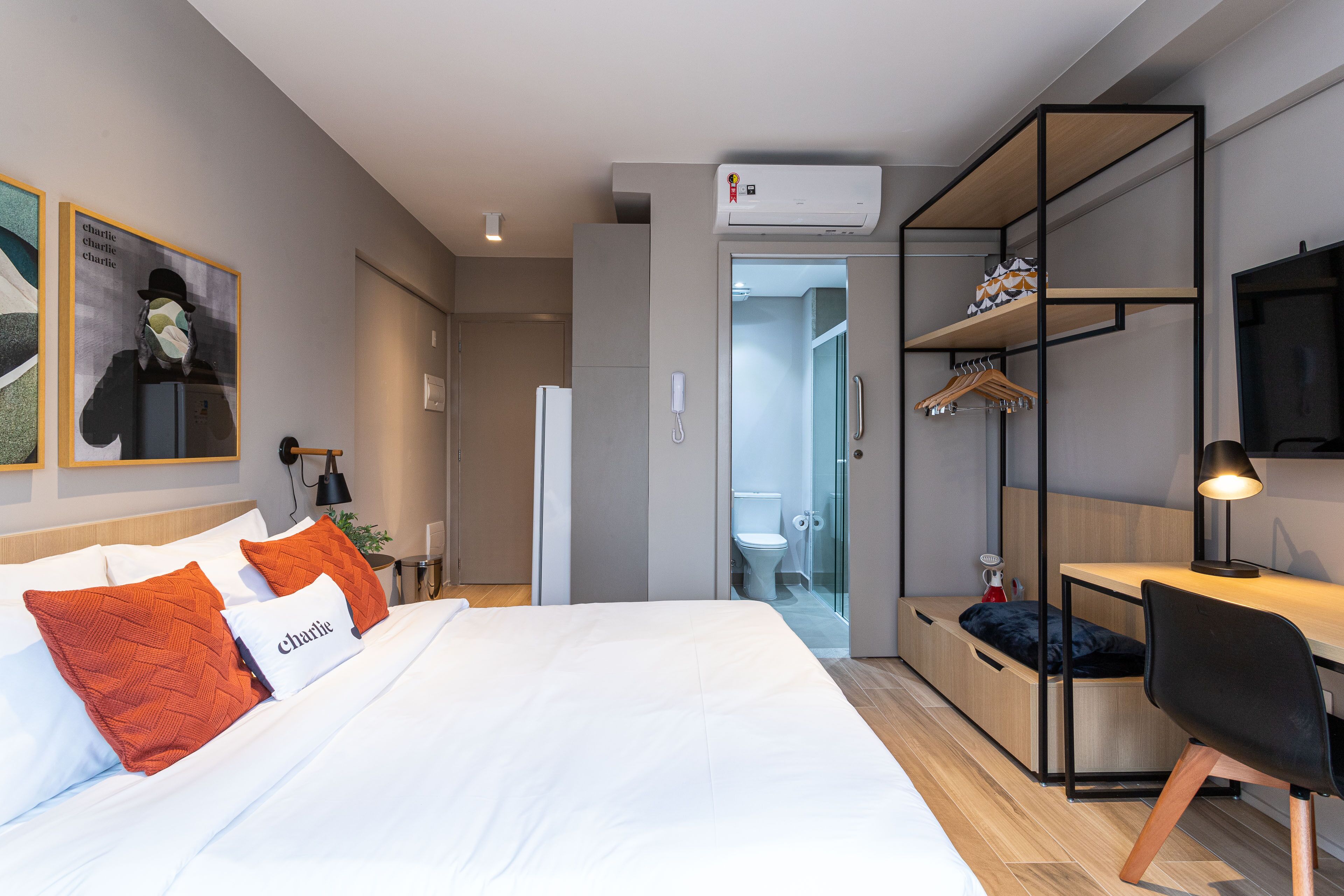 A modern hotel room with a bed, a desk, a wardrobe, and a shower area.
