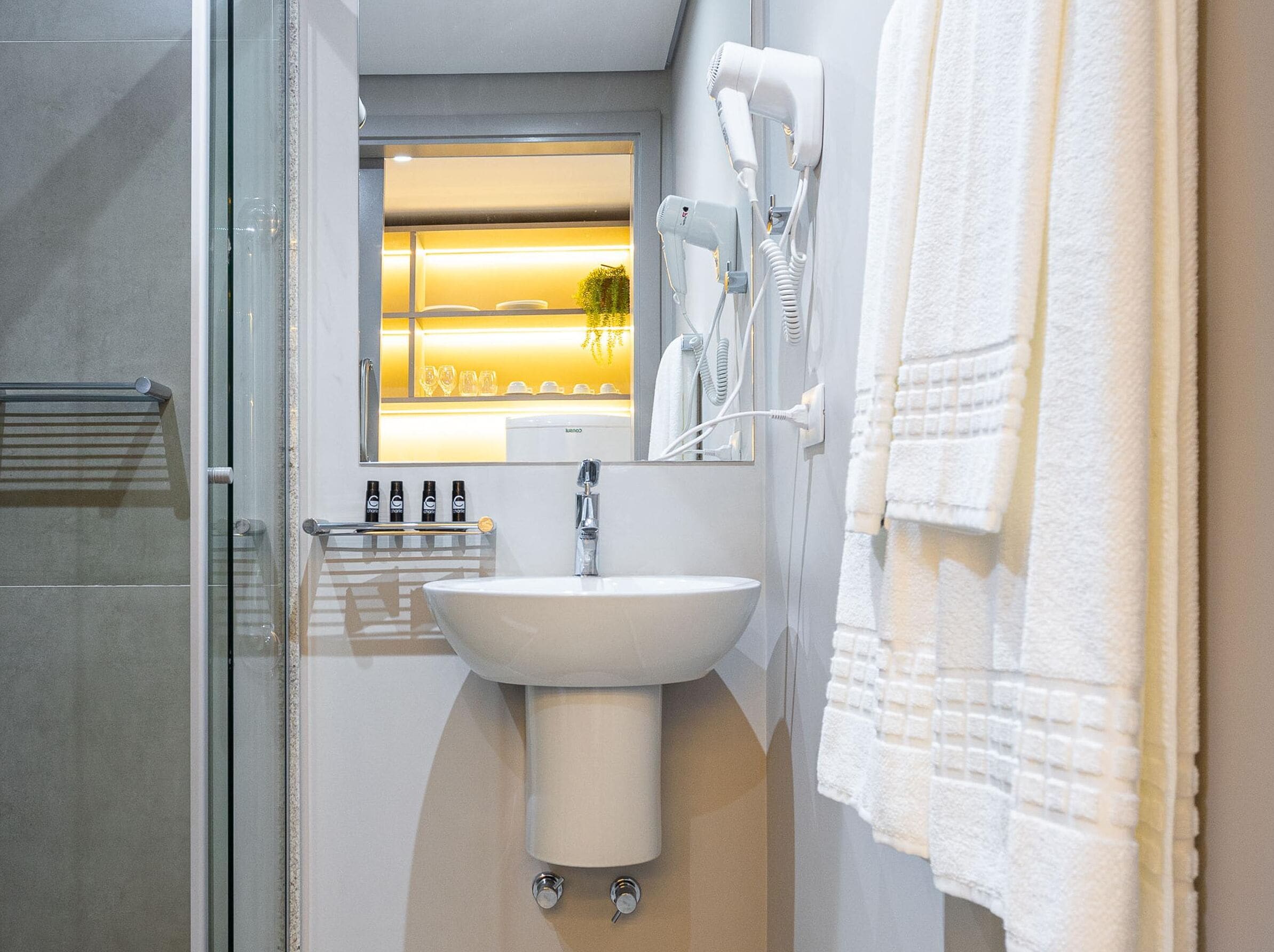 A modern bathroom with a glass shower enclosure, a white sink, and a hairdryer mounted on the wall.