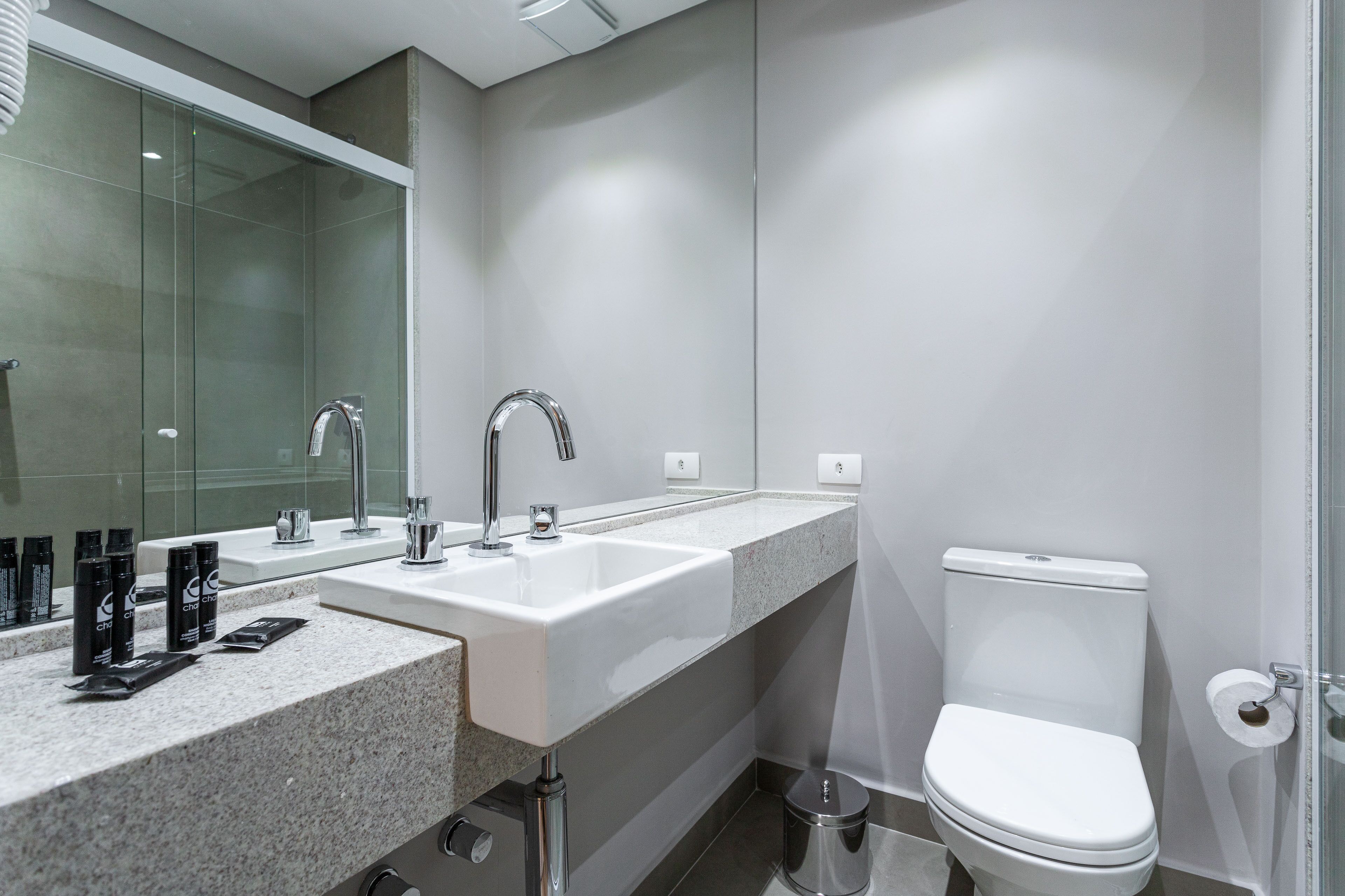 A modern bathroom with a double sink, a toilet, and a glass shower enclosure.