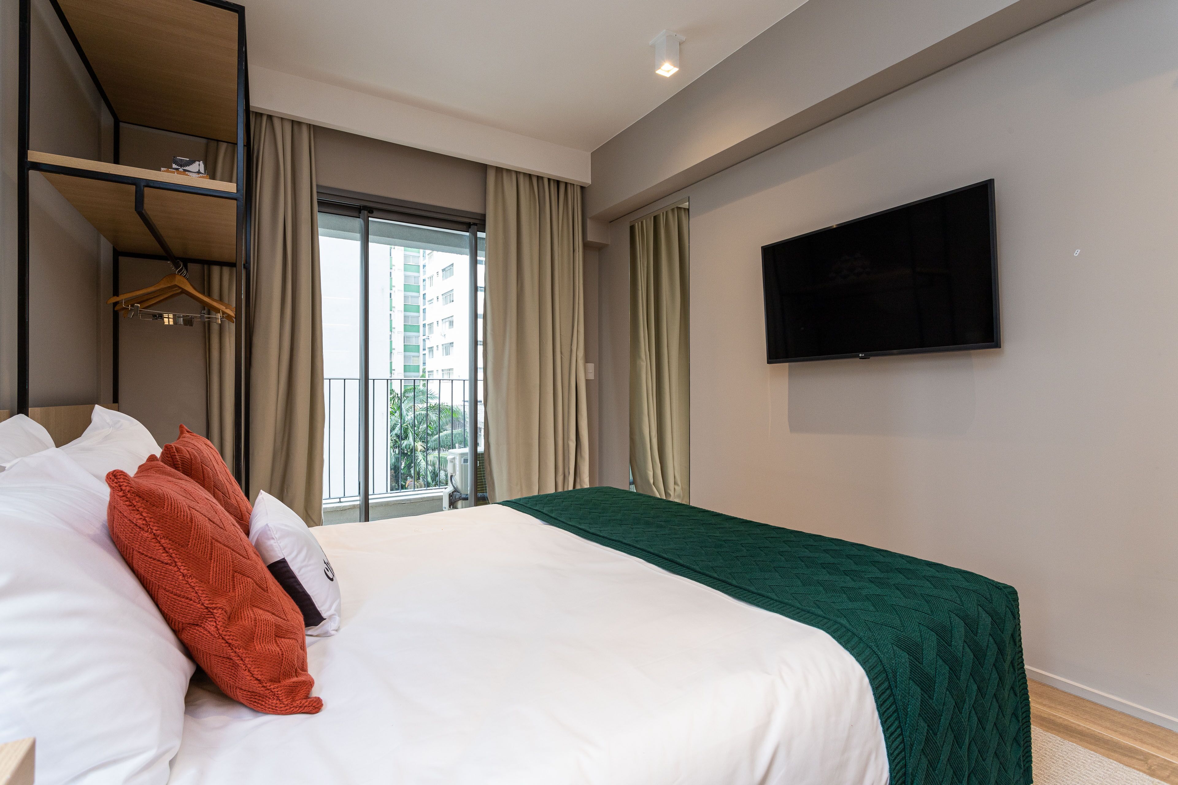 A hotel room with a bed, a TV mounted on the wall, and a window with curtains.