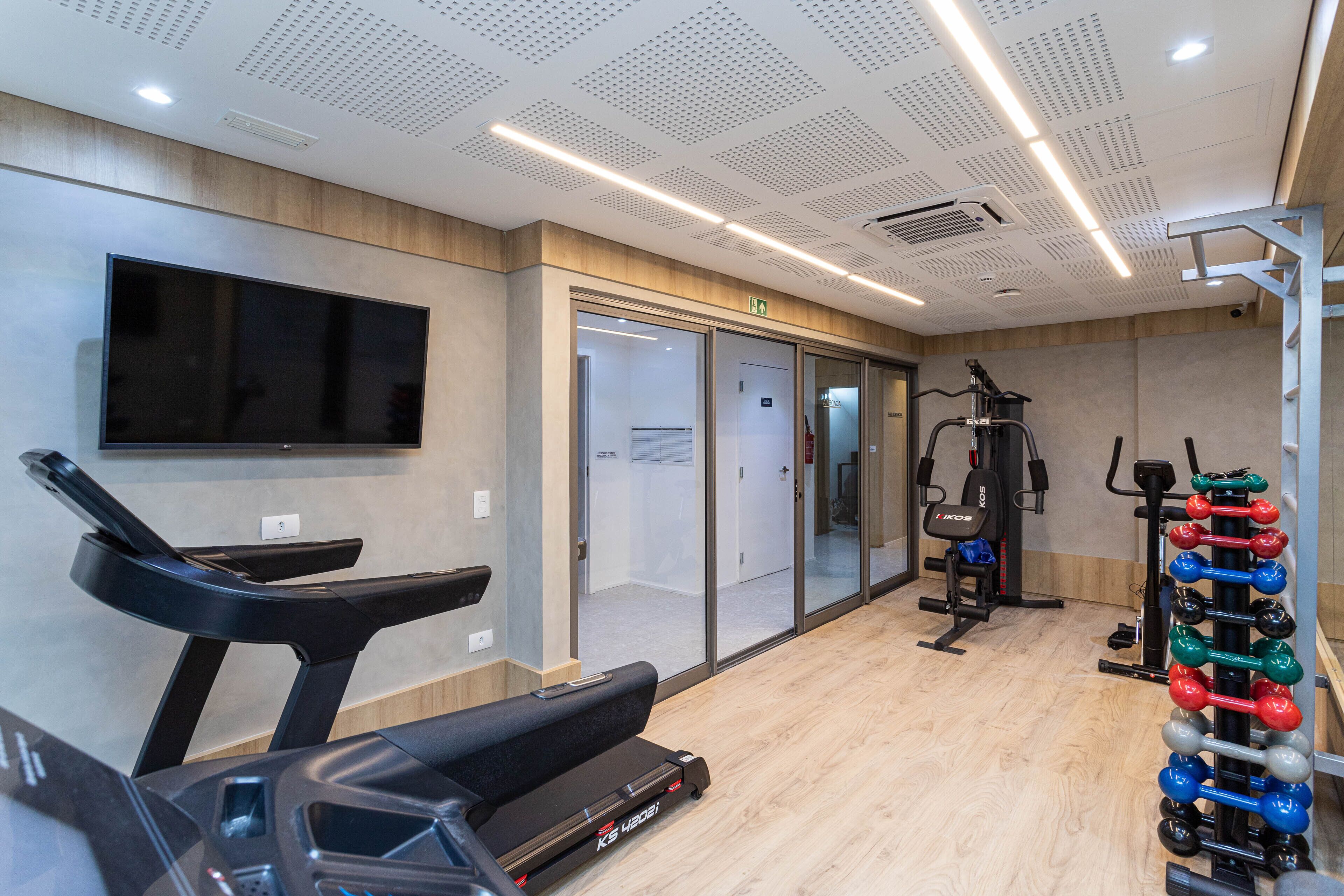 Un centre de remise en forme équipé de tapis de course, d’un téléviseur fixé au mur et d’un espace dédié à la musculation.