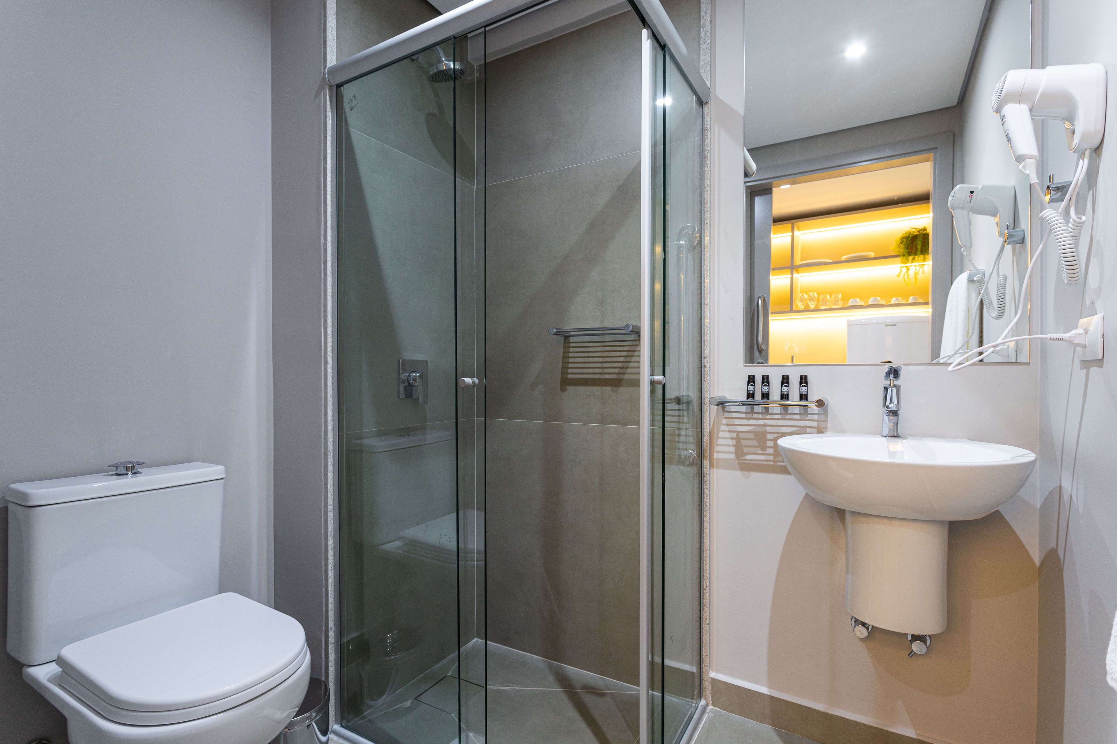 A modern bathroom with a glass-enclosed shower, a white toilet, and a sink with a mirror above it.