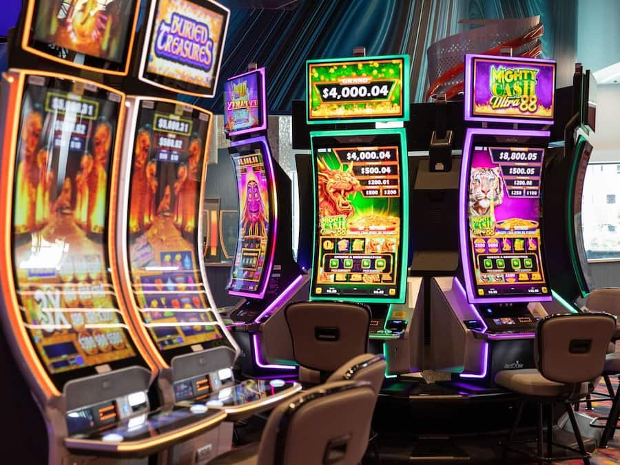 Una hilera de máquinas tragamonedas con diferentes denominaciones y temas, incluyendo una máquina 'Mighty Cash'.