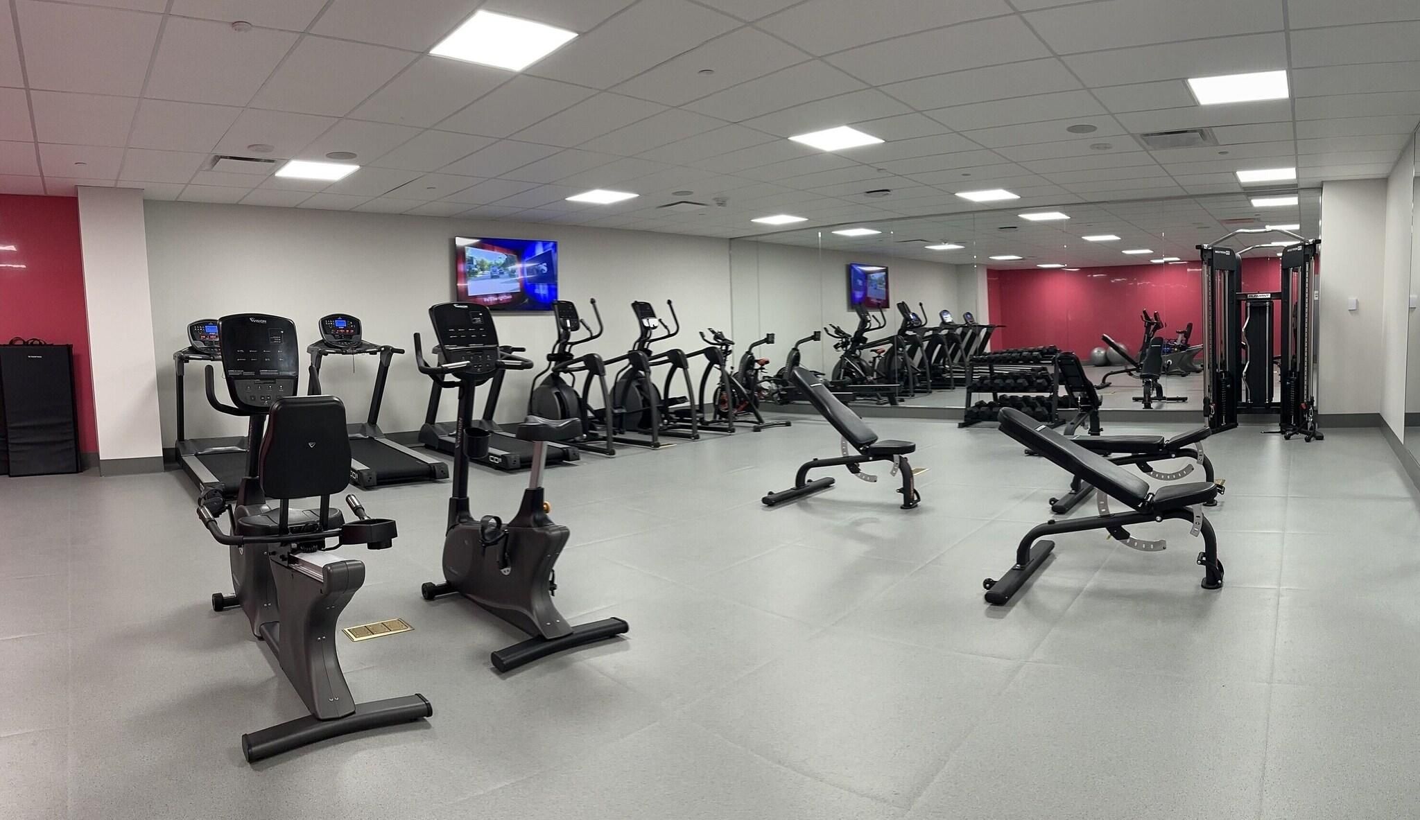 Een sportschool met diverse fitnessapparaten, waaronder loopbanden, hometrainers en krachttoestellen.