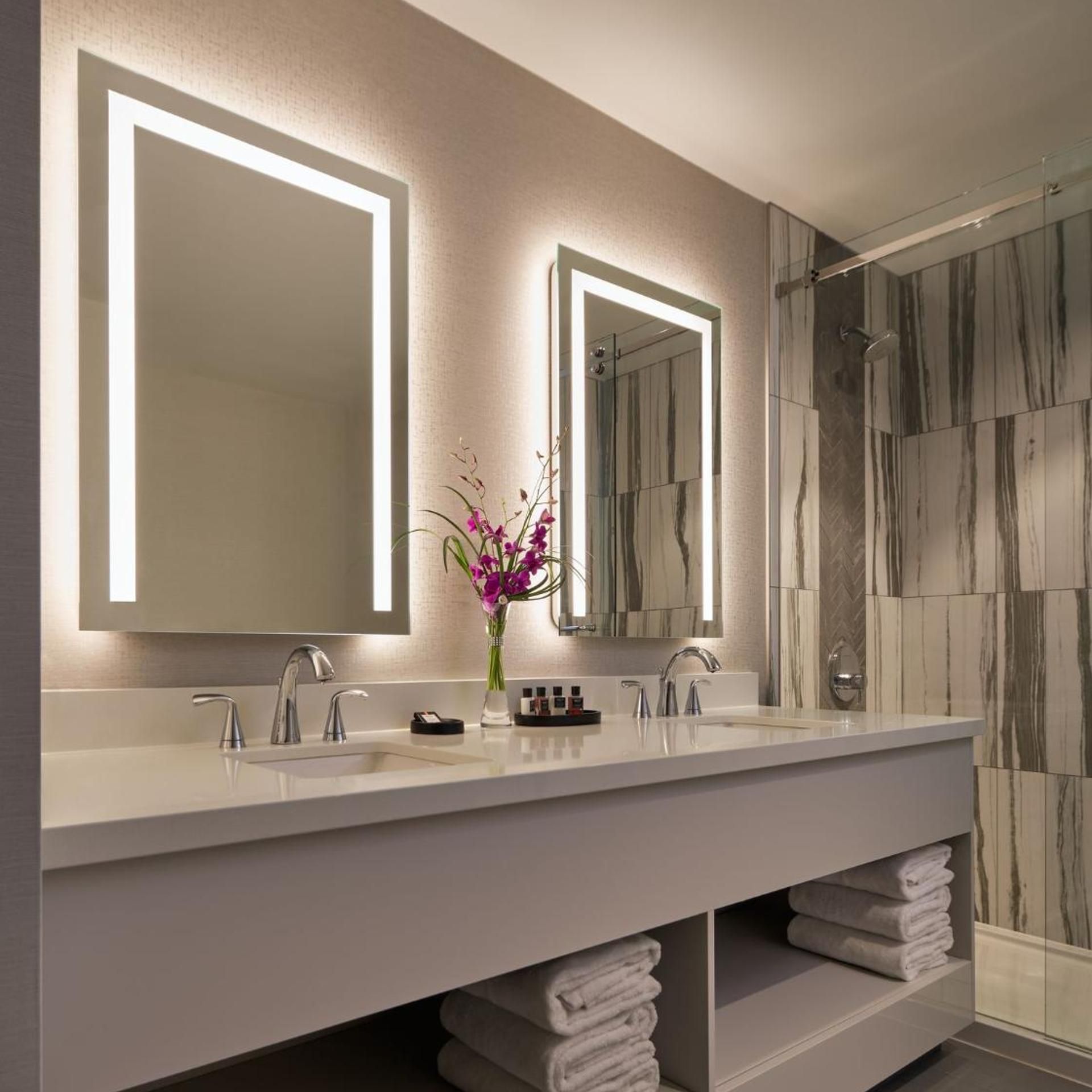 A modern bathroom with two sinks, a large mirror, and a shower area.